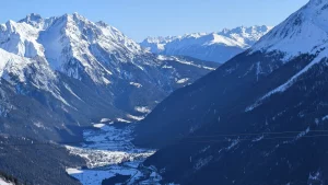 Verschneites Tal, vereinzelte Häuser und Gebirgszüge in der Ferne